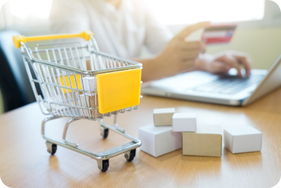 Mini shopping cart and boxes besides a laptop with online payment, Shopify Plus ecommerce solutions.